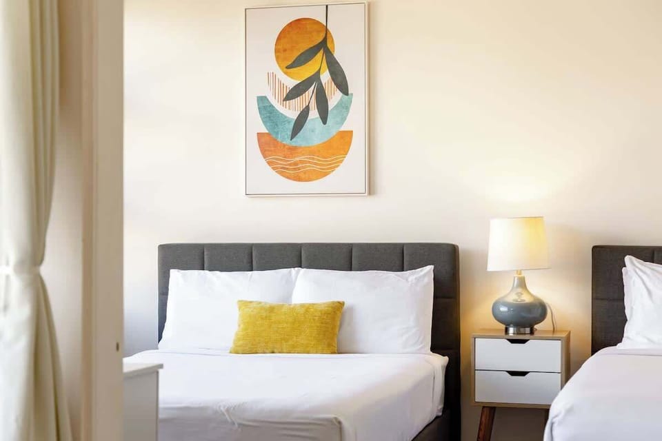 Modern bedroom with two beds, a bedside table, and abstract wall art.