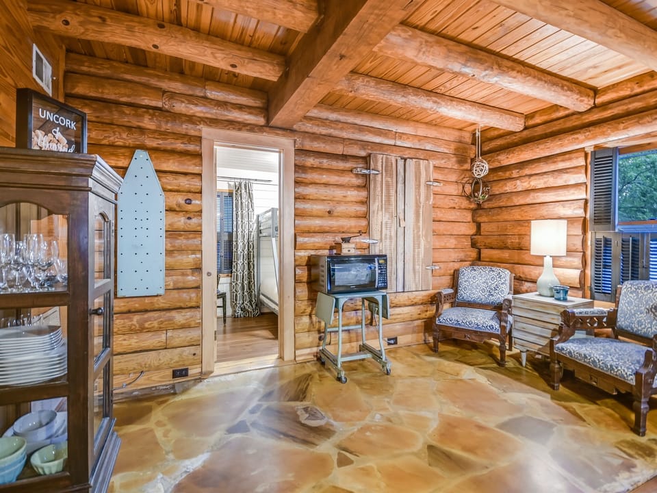 The Creek House gathering space next to the kitchen — coffee makers, prep counter, and dining for seven, all in one open log cabin layout.