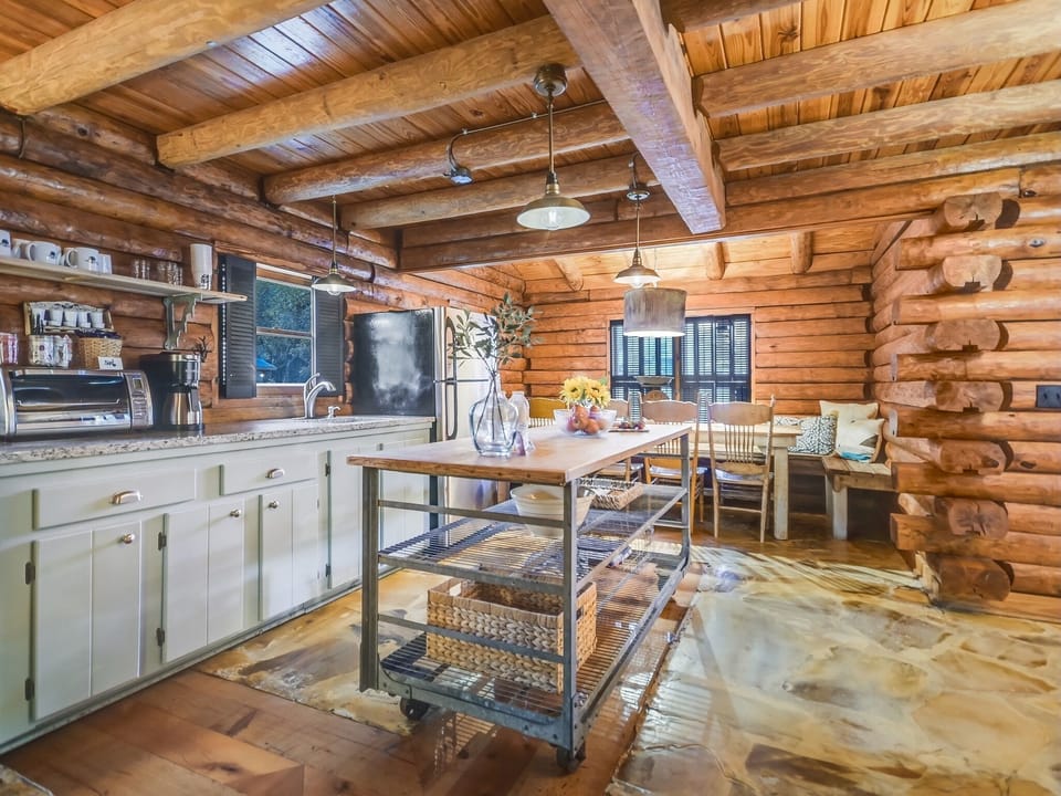 The gathering space next to the kitchen — coffee makers, prep counter, and dining for seven in one open log cabin layout.