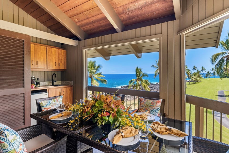 A table set for six on the lanai, ocean framed just past the railing.