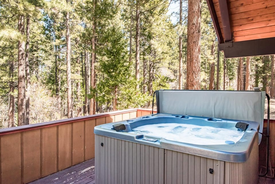 Outdoor hot tub with bubbling water on a wood-paneled deck surrounded by tall pine trees.