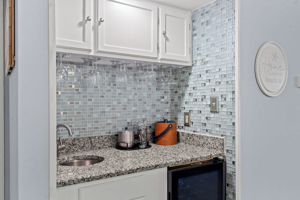 Enjoy easy entertaining with a wet bar featuring a chilled wine cooler, stylish glassware storage, and elegant coastal-inspired tilework that makes every moment feel like a getaway.