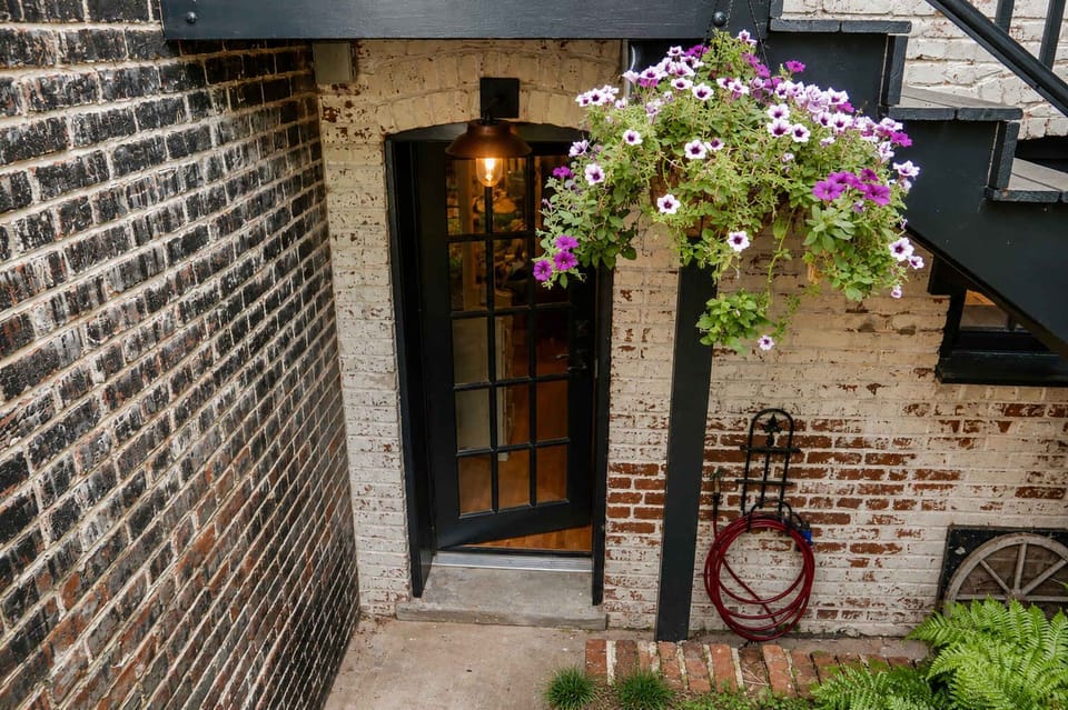 A charming private entrance tucked beneath the main house, with exposed brick, a welcoming glass-paneled door, and a beautiful hanging flower basket. This separate entrance leads directly into your cozy Capitol Hill cottage.