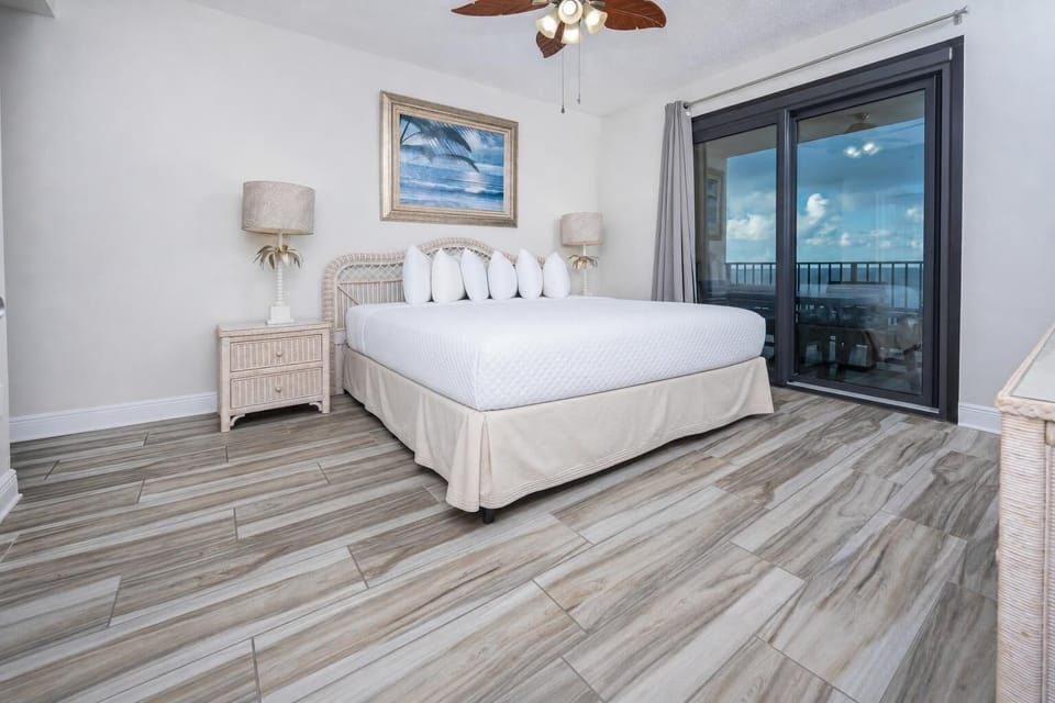 Master bedroom featuring a king bed, wicker nightstands, and sliding glass doors leading to a balcony beach view