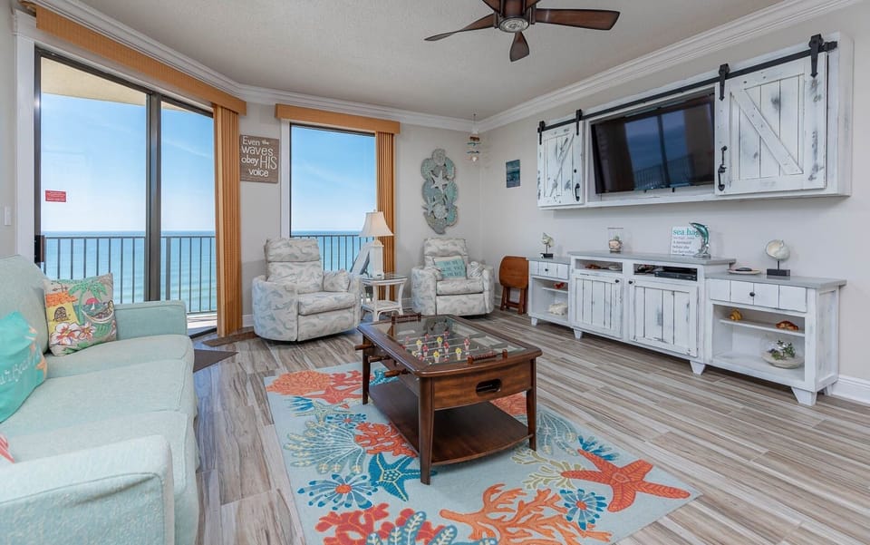 Cozy living area features a light blue sofa with queen sleeper, two chairs, and a beach view through balcony doors