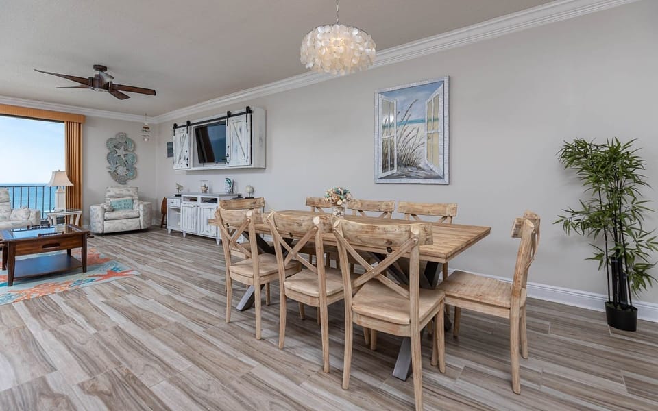 Brightly decorated living area features a wooden dining table, comfortable seating, and a stunning beachfront view