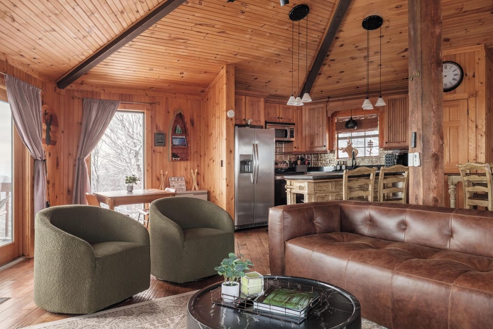 Gather around the stone fireplace with ample seating options in this open layout living area, framed by massive windows and direct deck access to stunning scenery.
