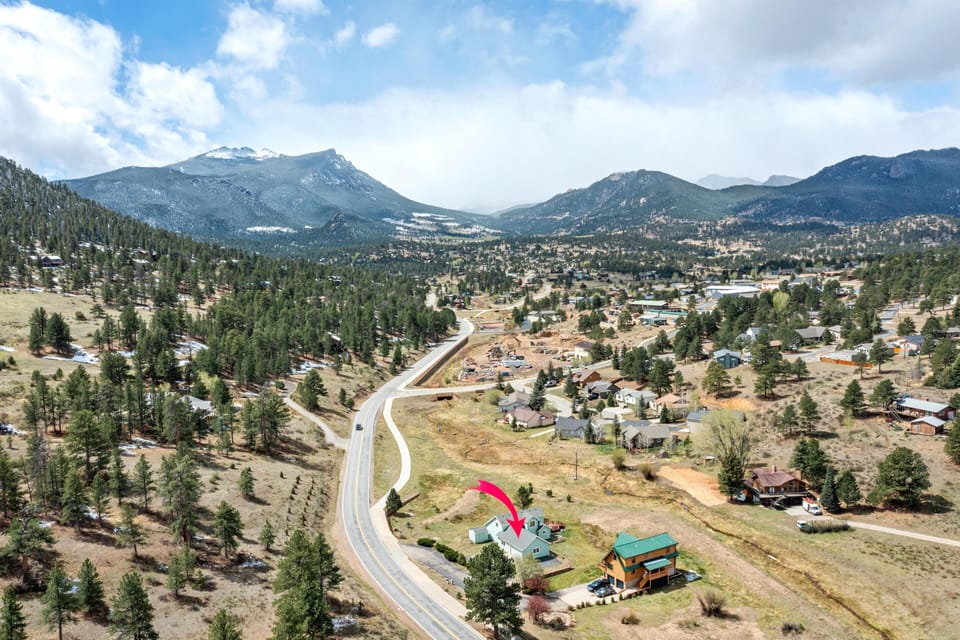 Aerial view of the neighborhood with a red arrow pointing to the light blue cabin near winding road and pine trees.