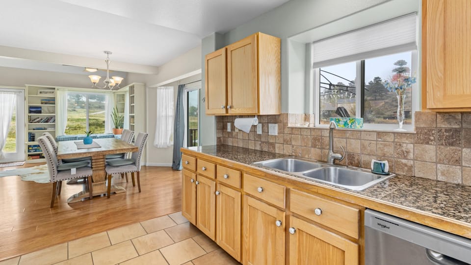 Granite countertops and tile backsplash line the kitchen with a double sink beneath a window overlooking the yard.