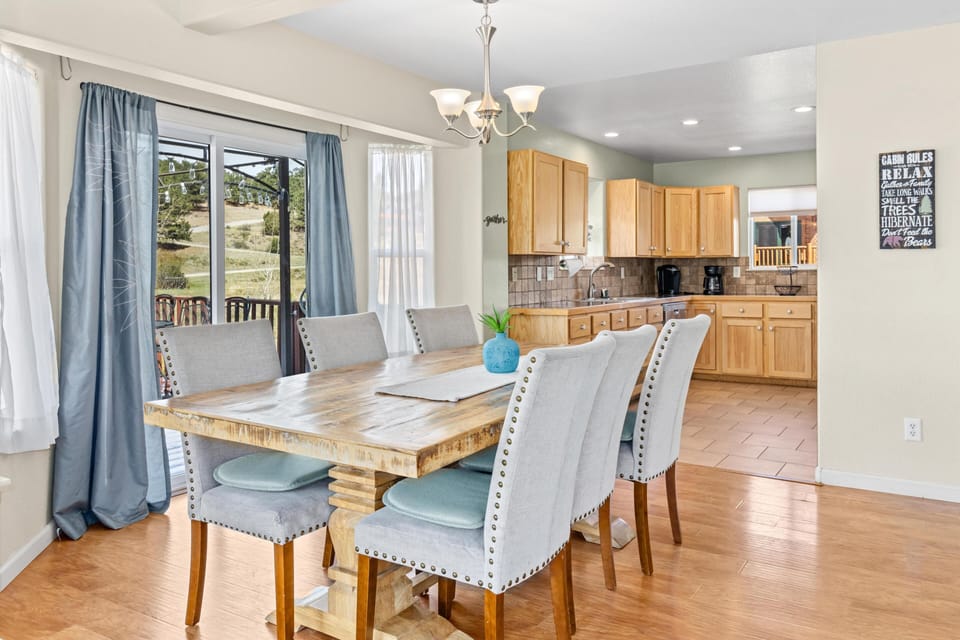 Dining area with a reclaimed wood table surrounded by gray upholstered chairs, sliding glass door, and light blue curtains.