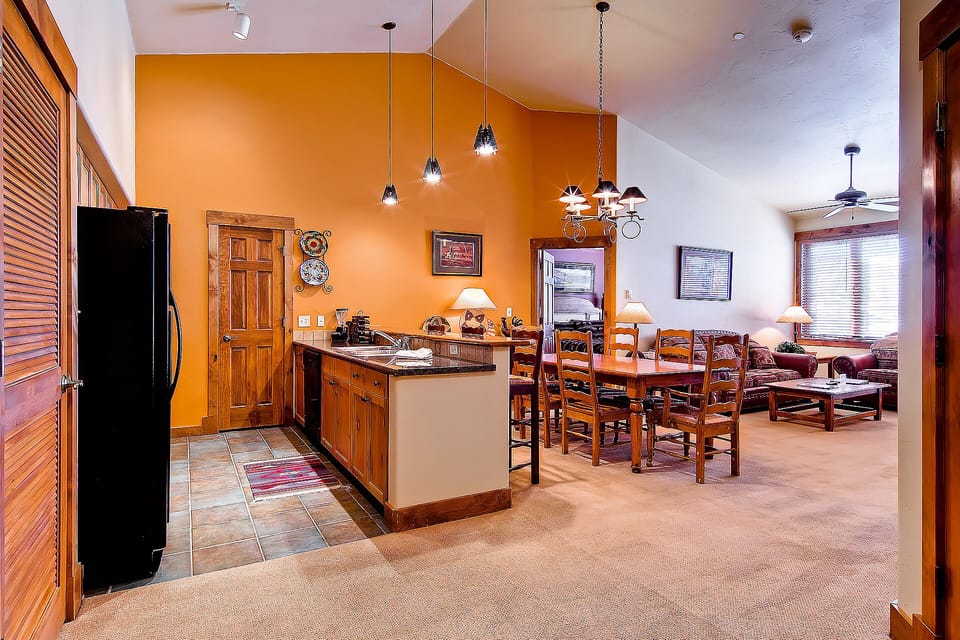 Your open-concept retreat blends kitchen and living beautifully with warm wood tones and vibrant orange walls creating a cozy mountain atmosphere.
