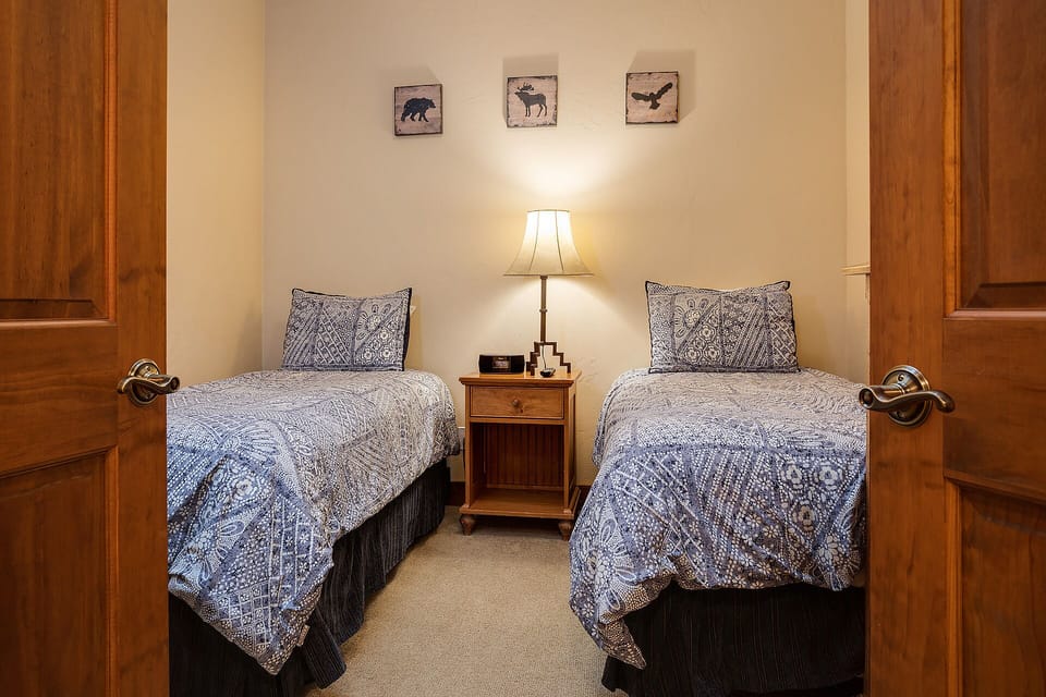 Cozy twin bedroom with rustic charm welcomes you with soft blue linens and warm wood accents for peaceful mountain retreat nights.