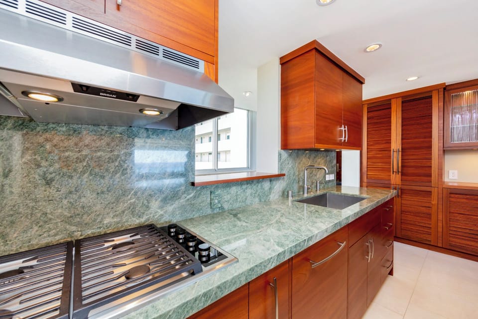 Kitchen - Gas cooktop and sink with gorgeous green granite that ideally contrasts with the dark teak wood cabinetry.