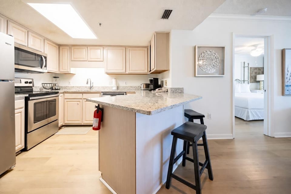 Bright kitchen features light wood cabinetry, granite countertops, coffee station, and breakfast bar with seating