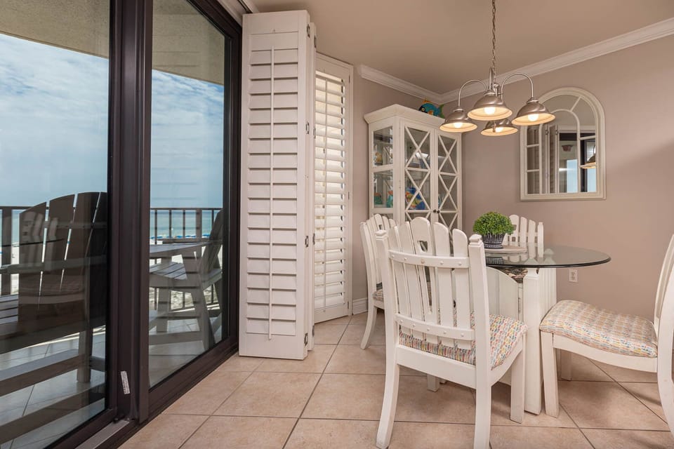 Dine in comfort at the glass-top table, surrounded by bright chairs and a view of the beachfront balcony