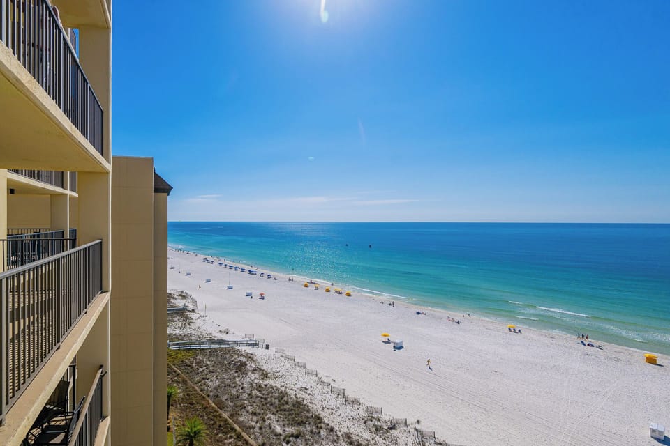 Sunlight sparkles on the calm coast as you stroll along the shore lined with colorful beach umbrellas