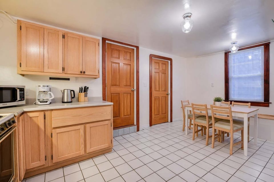 A bright eat-in kitchen with wood cabinets, tiled floors, dining table, and essential appliances, accented by warm trim and ample natural light.
