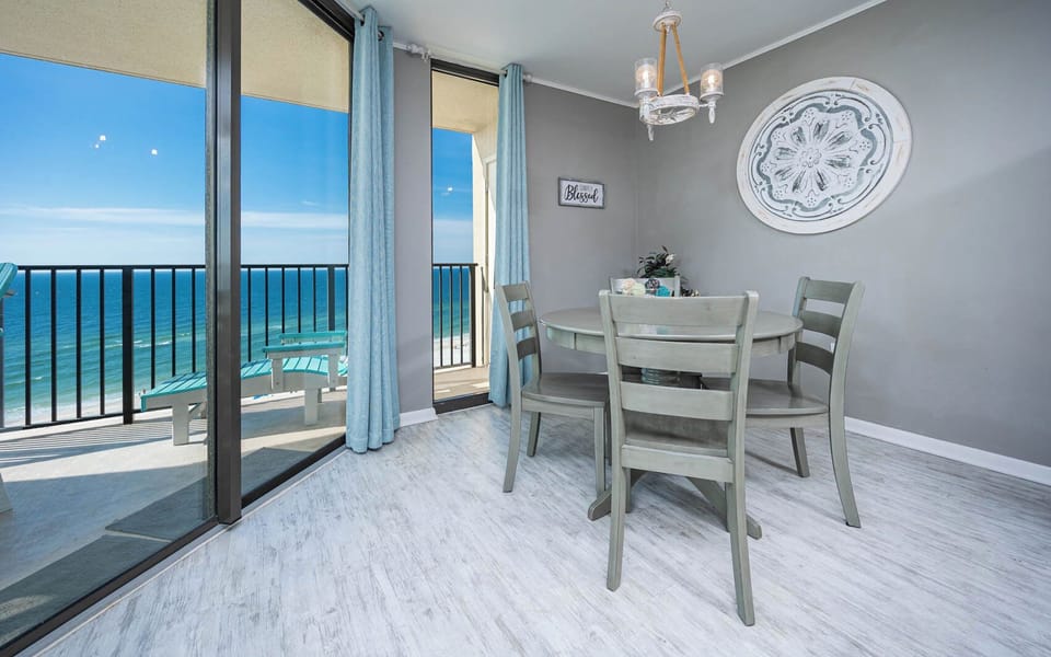 Bright dining area with a round table, four chairs, and a stunning beach front view through large glass doors