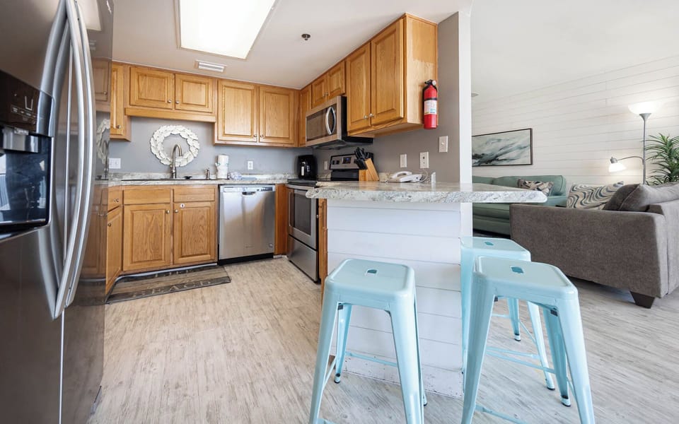 The fully-equipped kitchen features warm wooden cabinetry, a stylish countertop, and a breakfast bar with blue stools