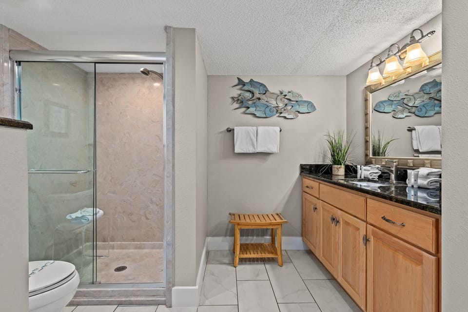 The spacious ensuite bath offers a bright, comfortable retreat with an oversized walk-in shower, generous vanity space, and a clean coastal feel—perfect for getting ready for the day or unwinding after time in the sun.