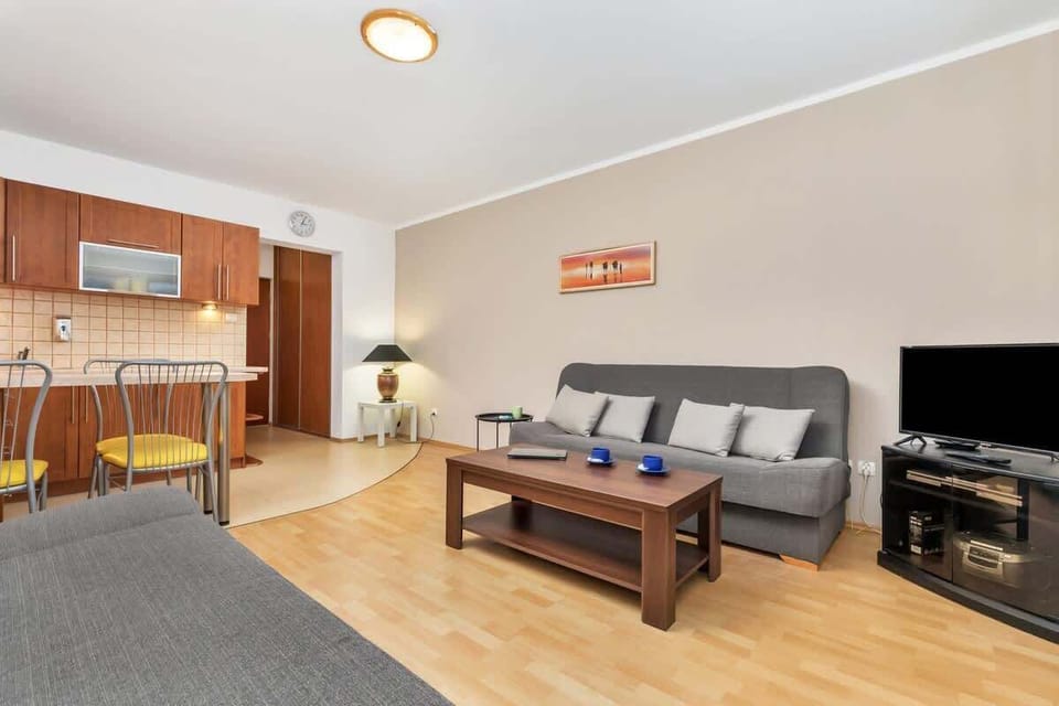 A view of the open-plan living and dining area, with a comfortable grey couch, a wooden coffee table, and a small dining area with a modern table and chairs in the corner.