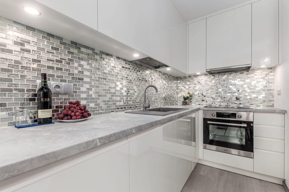 A sleek, modern kitchen featuring white cabinets, stainless steel appliances, and a backsplash of reflective silver tiles, adding a sense of depth and luxury.