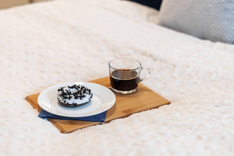 A close-up of a breakfast tray with a bowl of fruit and coffee, placed on soft bedding, creating a cozy, inviting morning scene.