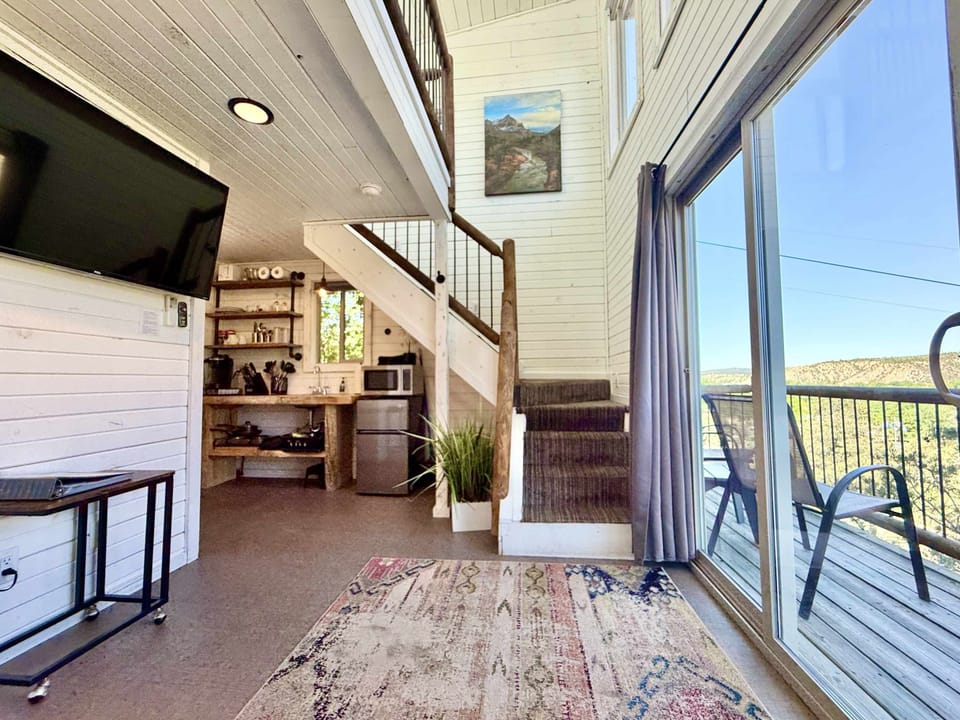 Treetop cabin interior with loft sleeping space, flat-screen TV, private bathroom, kitchenette, and cozy living area. Balcony and deck area with outdoor dining space, giving you a peaceful place to enjoy the views from your Treetop cabin.