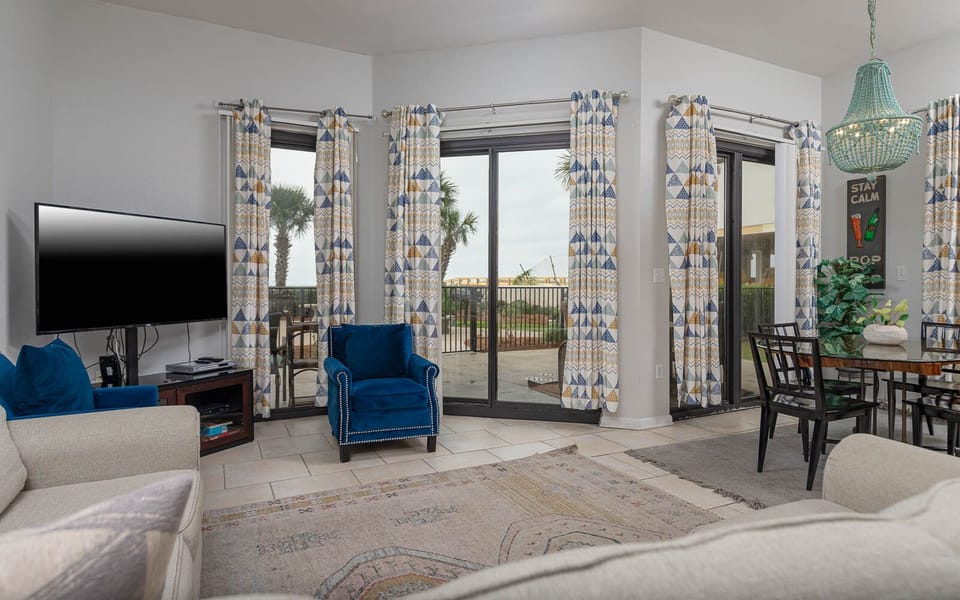 Relax in the inviting living area with a large TV, comfortable seating, and views of palm trees beyond the patio
