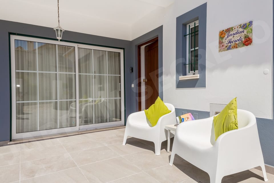 Front terrace entrance of Jardim Secreto villa in Carvoeiro, featuring large sliding glass doors, modern white seating with colourful cushions, and the villa name sign on the exterior wall