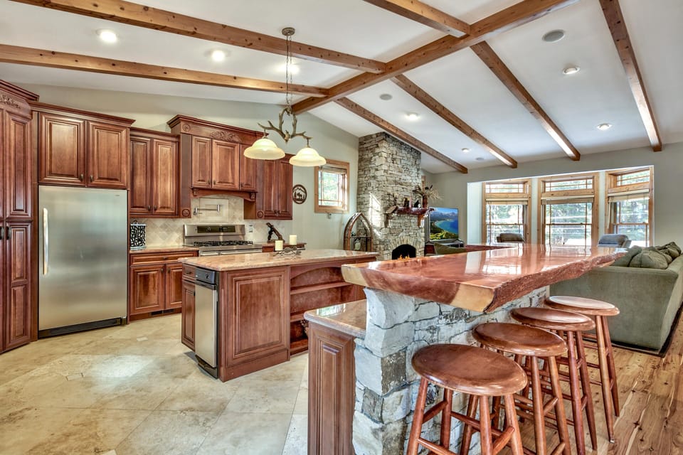 Gather around this stunning kitchen with rich wood cabinetry, stone fireplace, and spacious island perfect for memorable meals together.