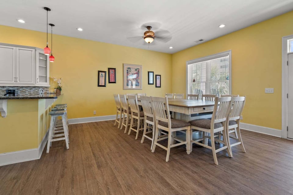 Dining table with white chairs under yellow walls at Another Day in Paradise, a 6-bedroom Cherry Grove rental