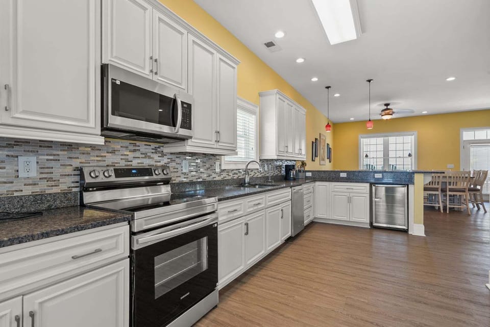 White cabinetry and an island with seating at Another Day in Paradise, a 6-bedroom Cherry Grove vacation rental