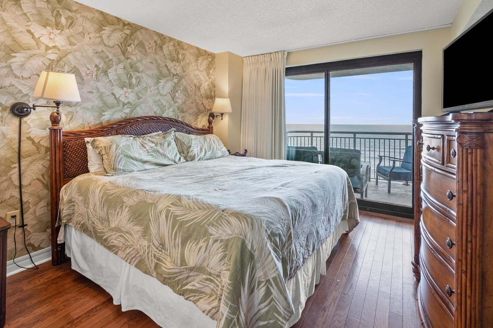 Bedroom with ocean views, a wall-mounted TV and doors opening to the balcony at Windemere 703, Ocean Drive