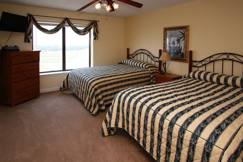 Two beds with striped covers and a dresser TV at Beachwalk Villas 701, a Cherry Grove vacation rental