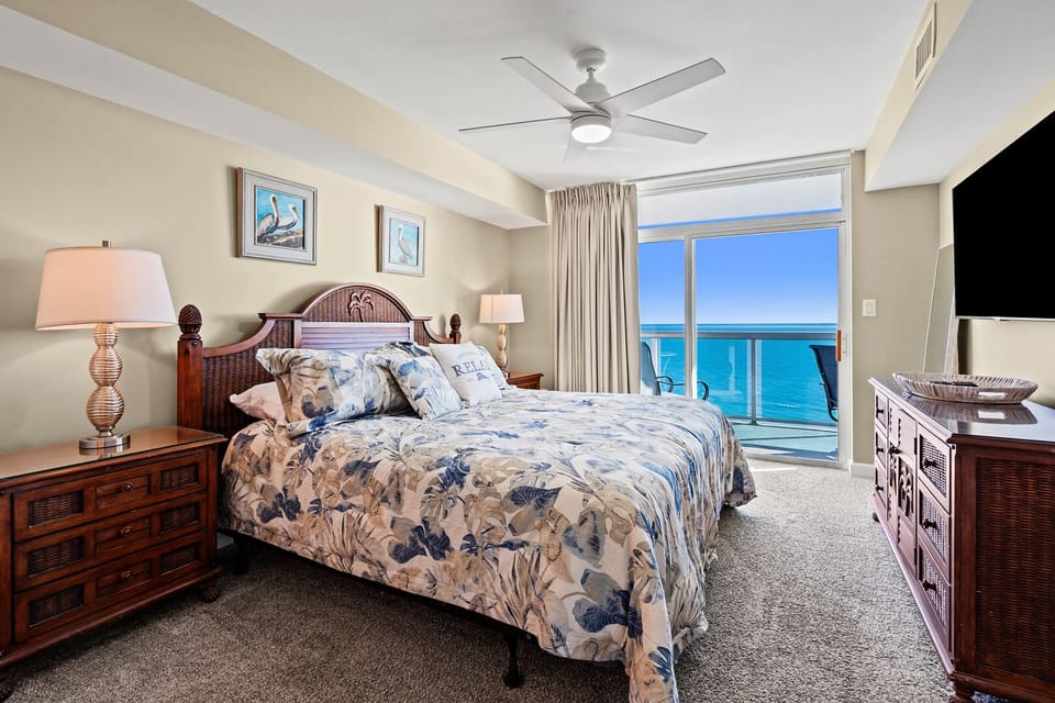 Bedroom with floral bedding and a sliding door to the ocean-view balcony at Laguna Keyes 1104, Cherry Grove