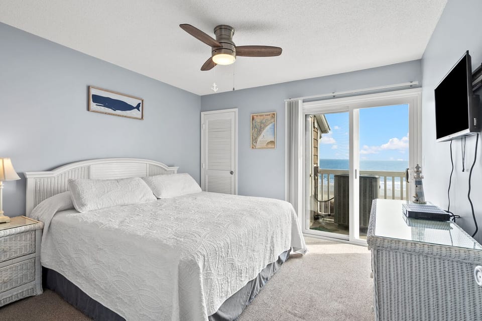 Bedroom with a ceiling fan, TV and a sliding door to the ocean-view balcony at Raintree Villas 3F, Cherry Grove