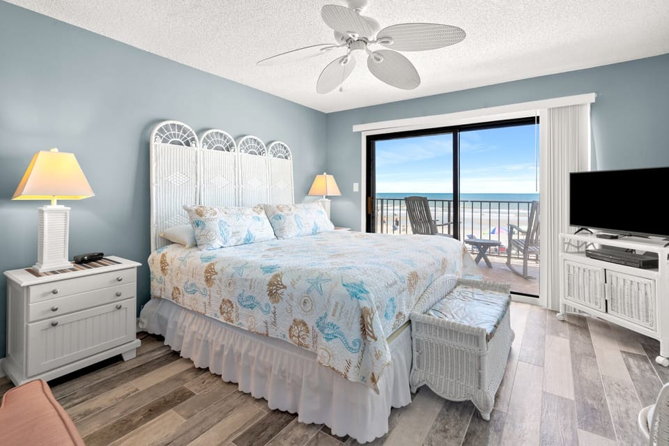 Bedroom with sea-themed bedding and sliding doors opening to the ocean-view balcony at Shalimar 1B