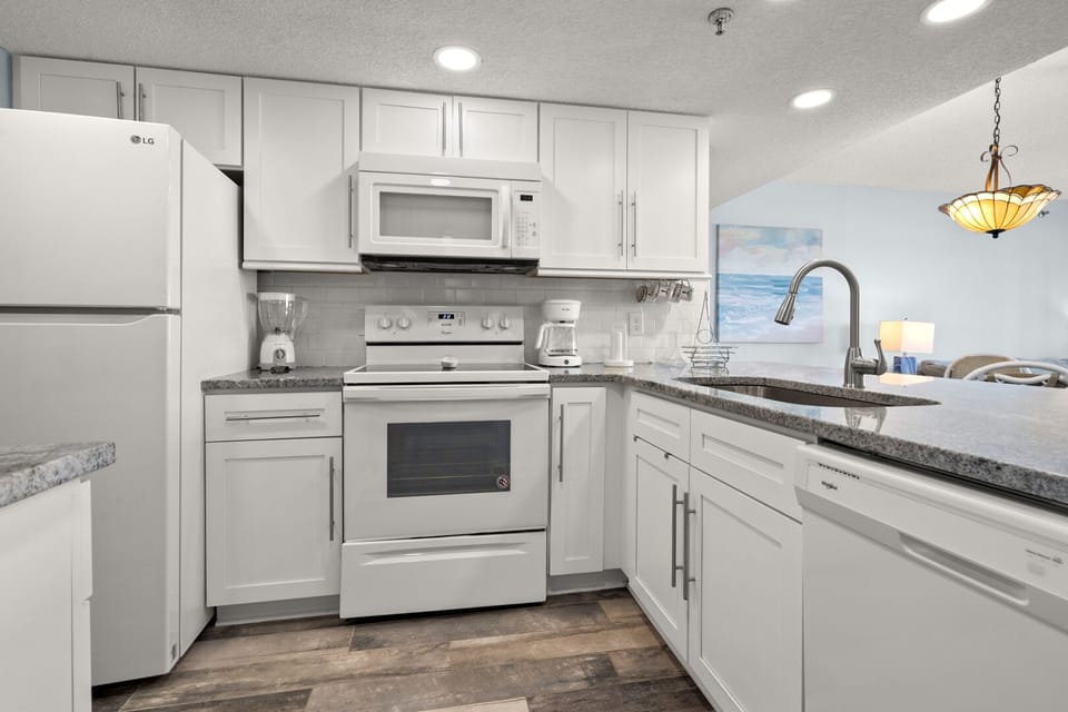 Kitchen with white cabinetry, a microwave above the range and a refrigerator at Shalimar 1B, Cherry Grove
