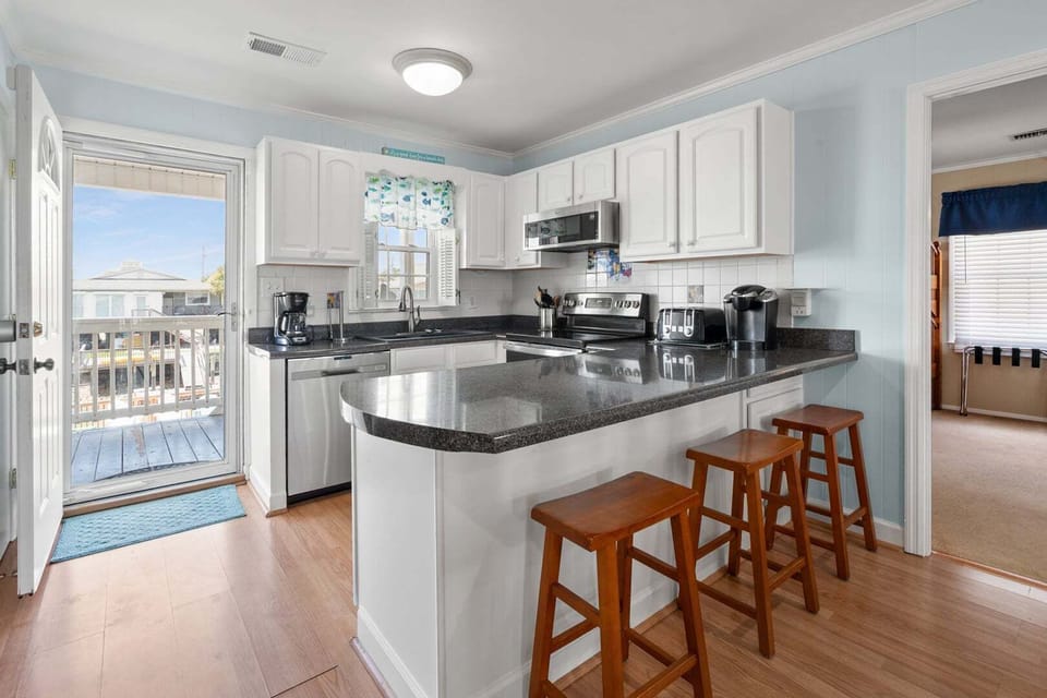 Kitchen island with bar stools and a door to the porch at Anchor in the Waves, a 4-bedroom Cherry Grove rental