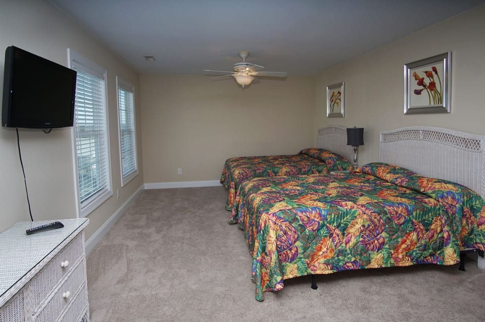 Two beds and a wall-mounted TV in a carpeted bedroom at West Winds II, a Crescent Beach vacation rental