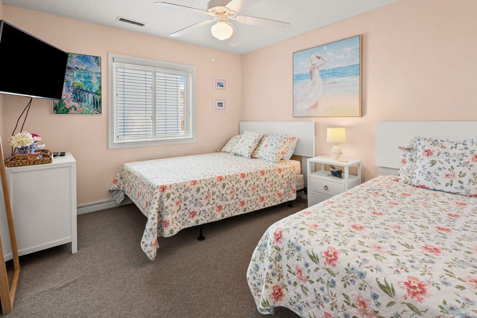Two beds with floral bedding in a soft pink bedroom at Surf Villas I B2 in Ocean Drive