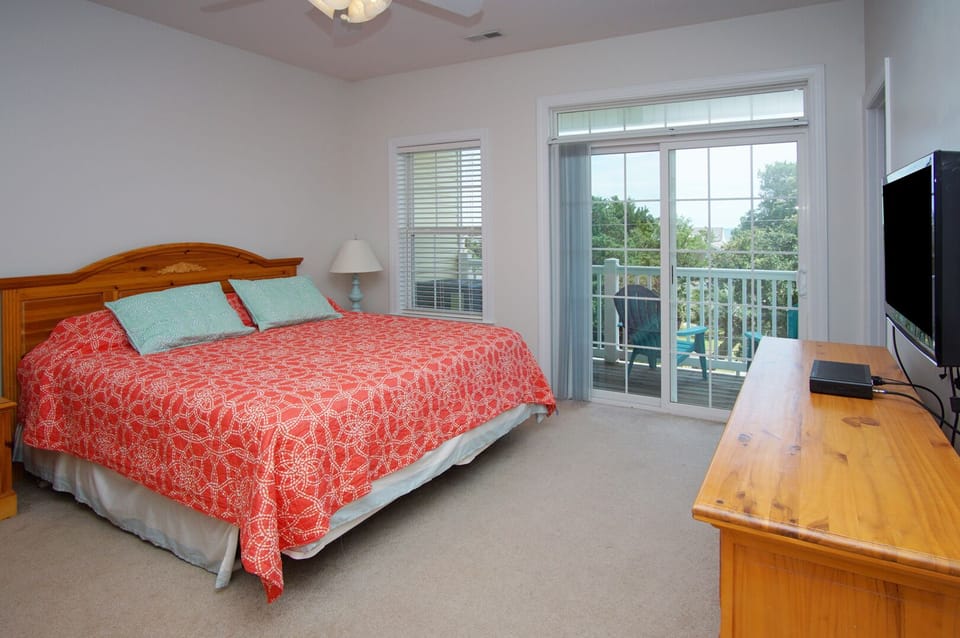 Bed dressed in red patterned bedding beside a balcony door at Palmetto Coast, Villa A, a 5-bedroom rental in Crescent Beach