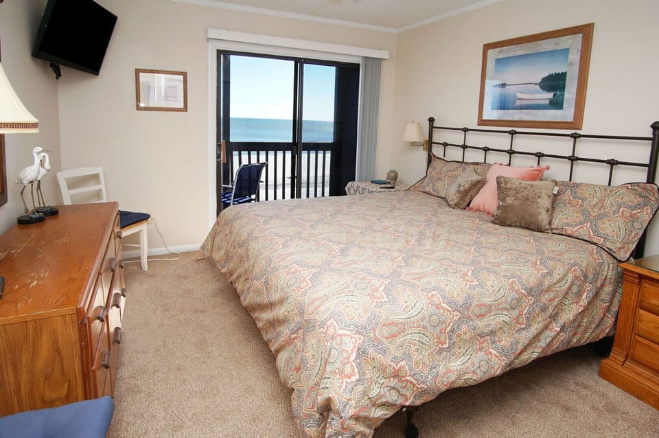 Bedroom with a wall TV and sliding door to the ocean-view balcony at Tilghman Beach & Racquet Club 328