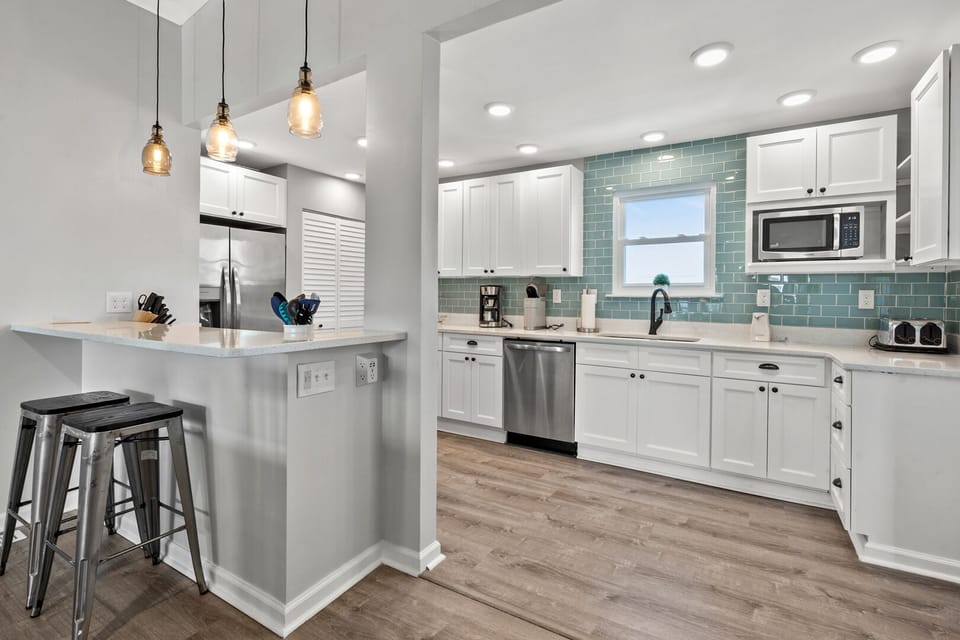 Kitchen with white cabinetry, a blue backsplash and an island with bar stools at Pelican's Perch, Cherry Grove