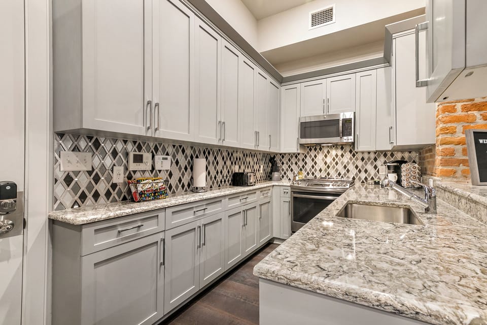Galley-style, fully equipped kitchen with an open flow to the living/dining area. Stocked with essentials from mixing bowls to wine glasses, featuring stainless steel appliances, a gas range, stone countertops, and a luxury tile backsplash!