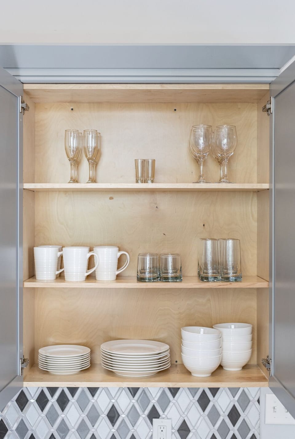 Galley-style kitchen open to living/dining area. Fully stocked with essentials from mixing bowls to wine glasses. Features stainless steel appliances, gas range, stone countertops, and tile backsplash, combining functionality with luxury.