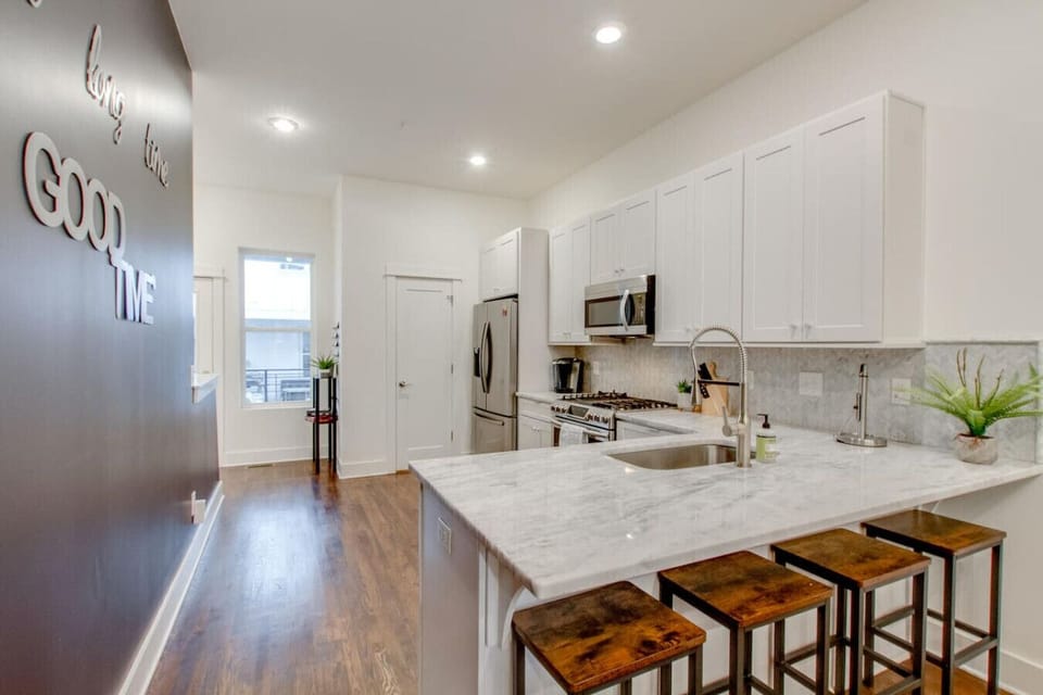 Kitchen with white cabinets, marble island with bar stools, and dark accent wall