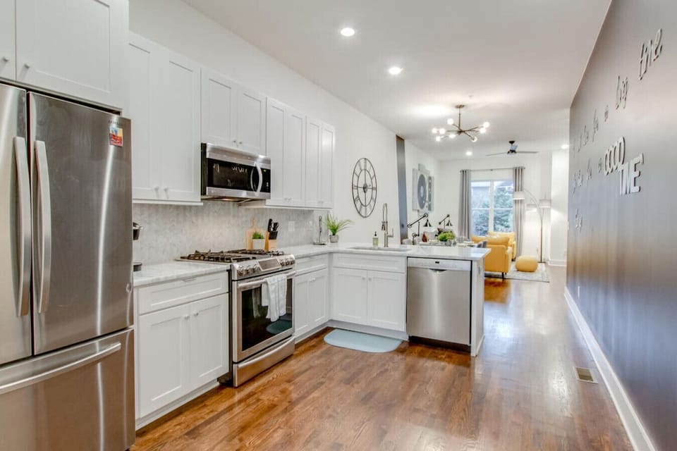 Bright kitchen with white cabinetry, stainless steel appliances, chandelier, and hardwood floors