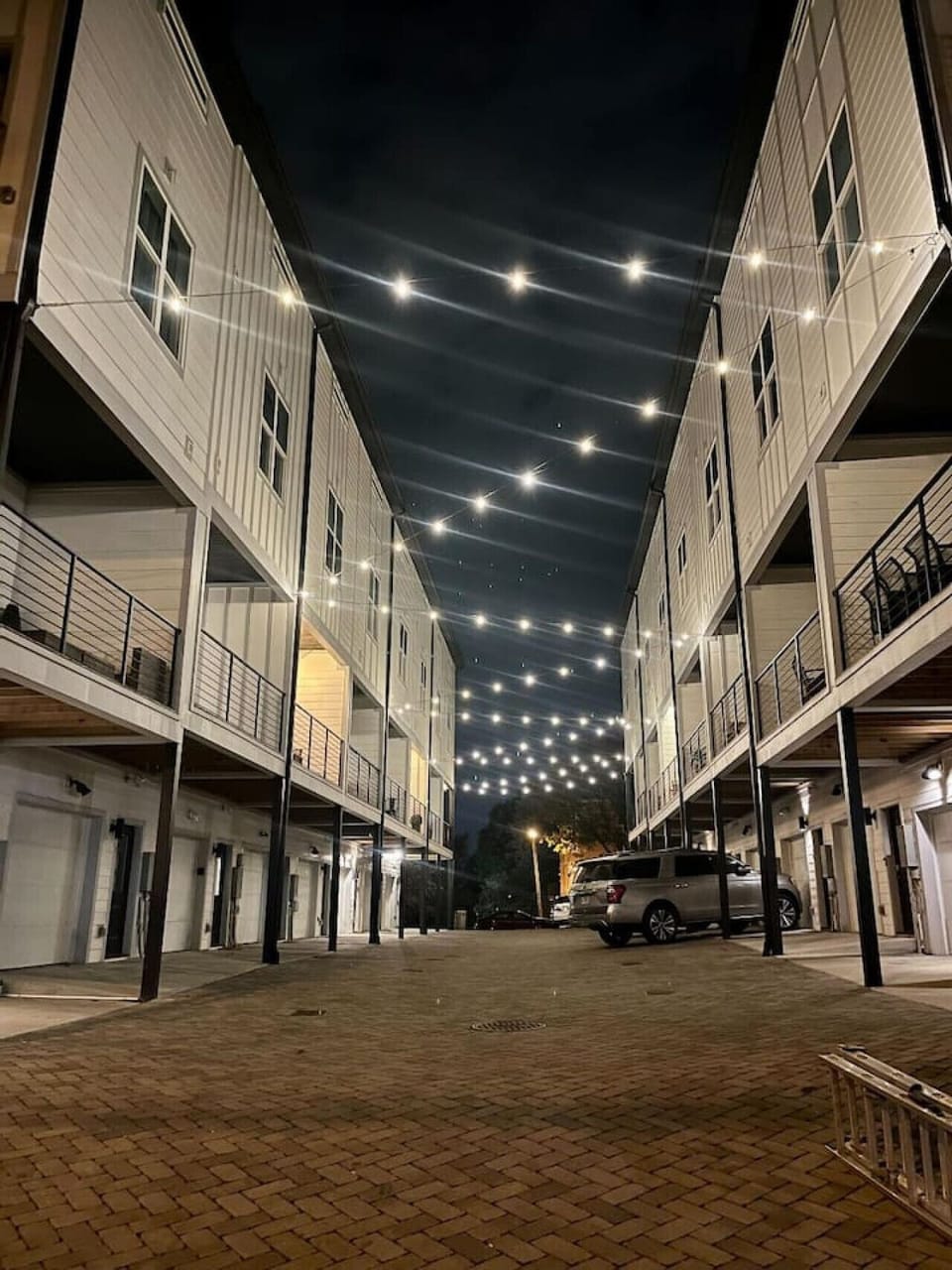 Exterior night view of townhouse complex with illuminated courtyard and string lights